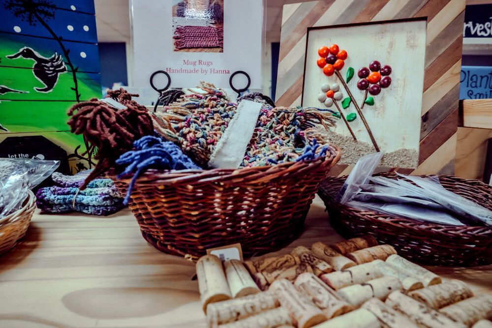 Wicker baskets with colorful craft supplies on a wooden table, next to corks and art.
