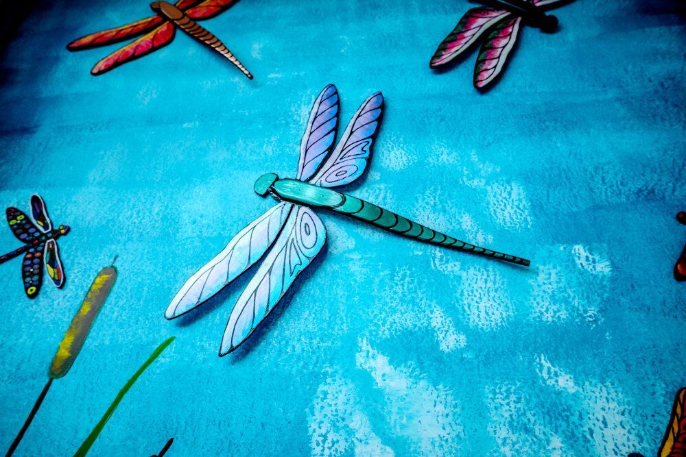 Dragonfly art on a textured blue background, with cattails, in various colors and sizes.