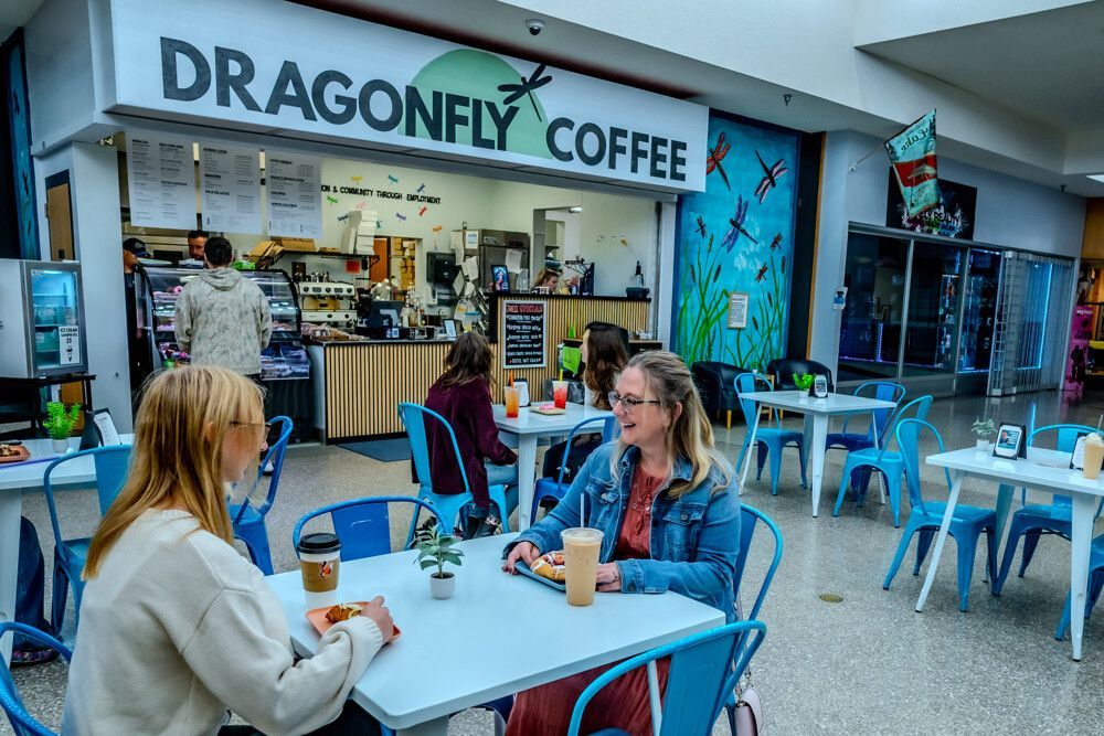 People at Dragonfly Coffee shop, seated at blue tables. Shop has a dragonfly mural.