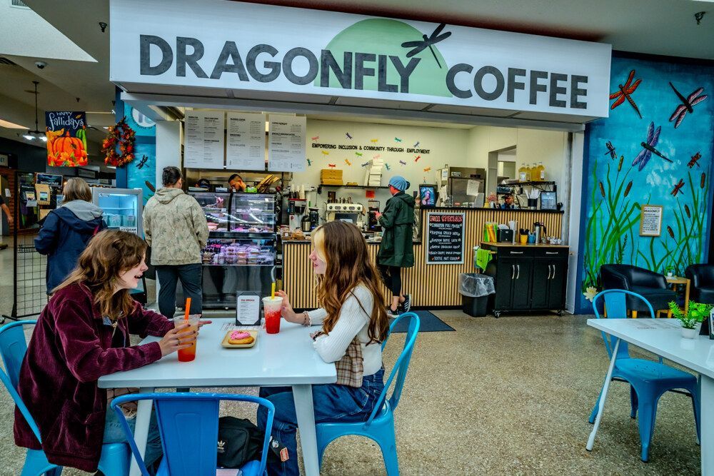 Dragonfly Coffee shop in a mall, two women at a table, customers in background, dragonfly mural.