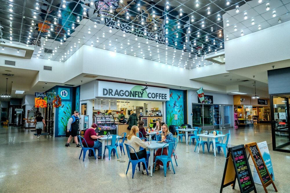 Dragonfly Coffee shop in a mall. People seated at blue tables, ordering. Overhead lights, mirrored ceiling.