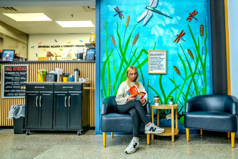 Woman reading in front of a mural of dragonflies and cattails; coffee shop setting.