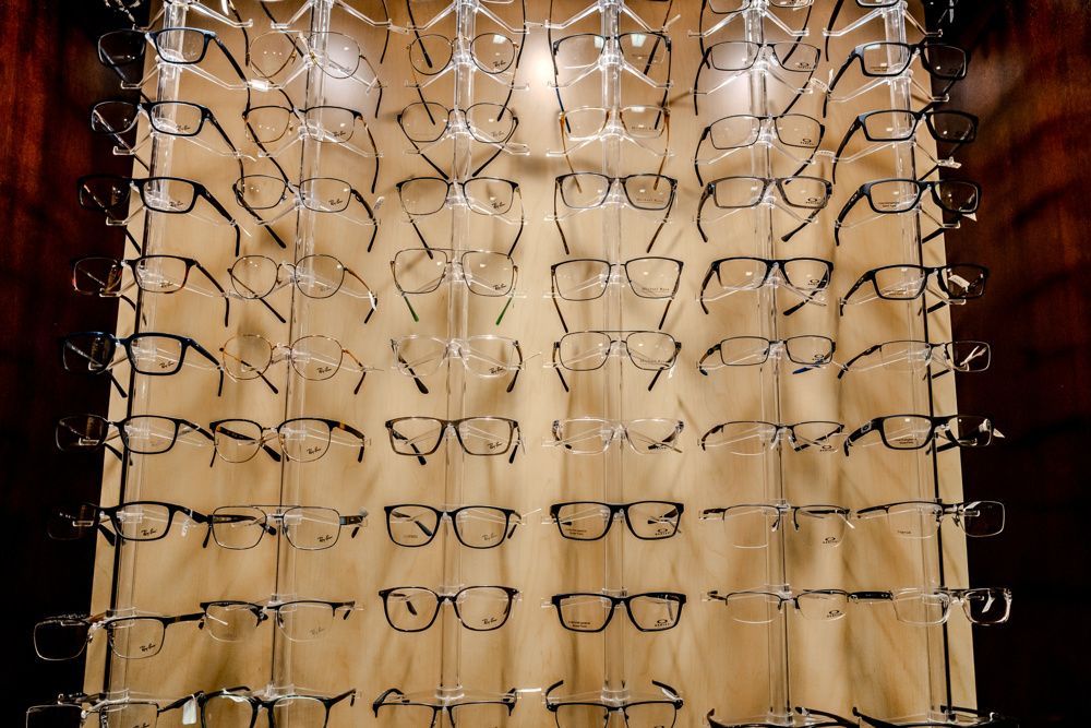 Eyeglass frames displayed on a hanging rack with a wooden background.