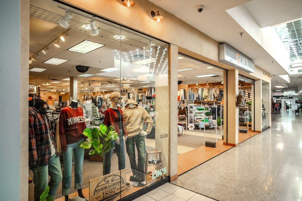 Clothing store storefront in a mall with mannequins in the window, showcasing apparel.