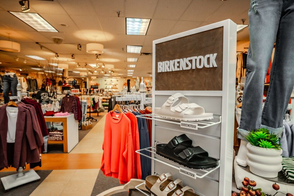 Birkenstock sandals display in a clothing store with apparel racks and bright lighting.
