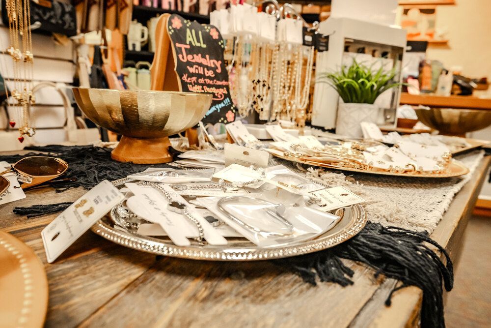 Jewelry display on a wooden table, featuring necklaces, bracelets, and earrings in a store setting.