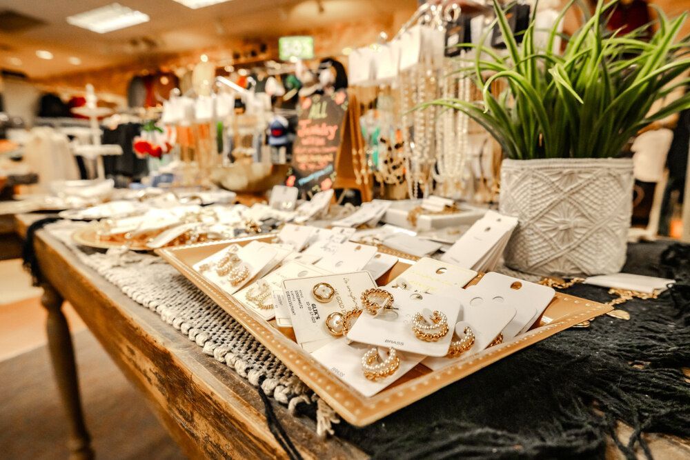 Jewelry display on wooden table in store, with earrings, necklaces, and potted plant.