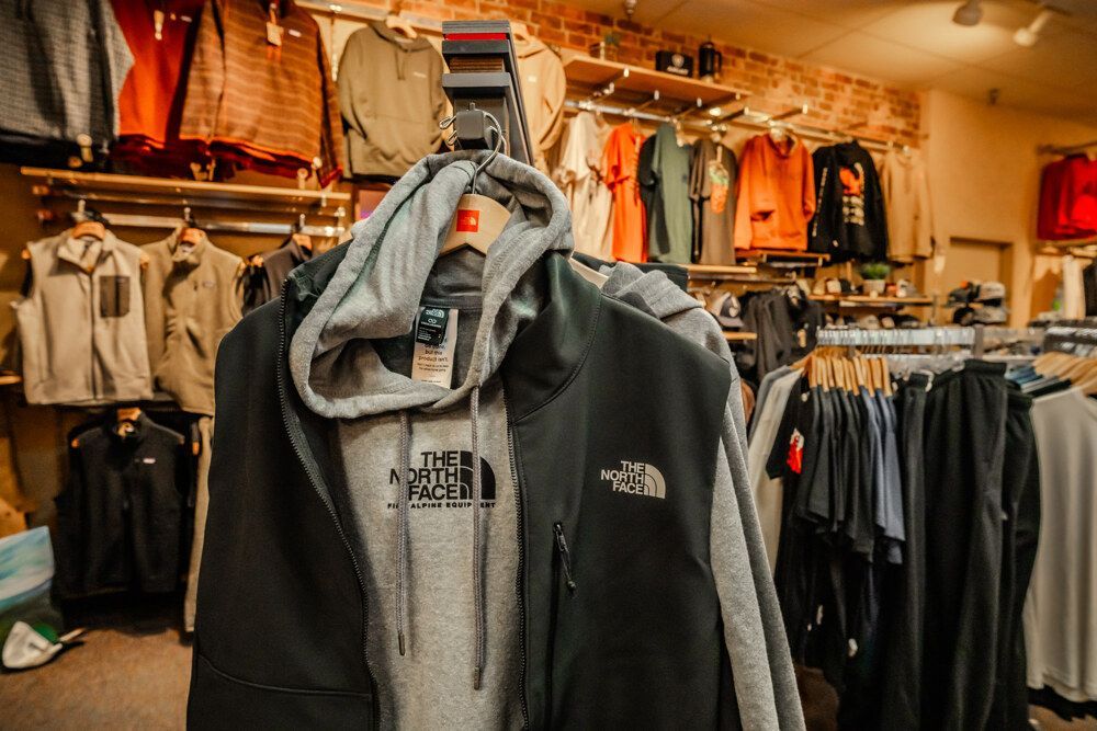 Clothing store interior with North Face jackets and hoodies on display. Wooden shelves and brick wall in the background.