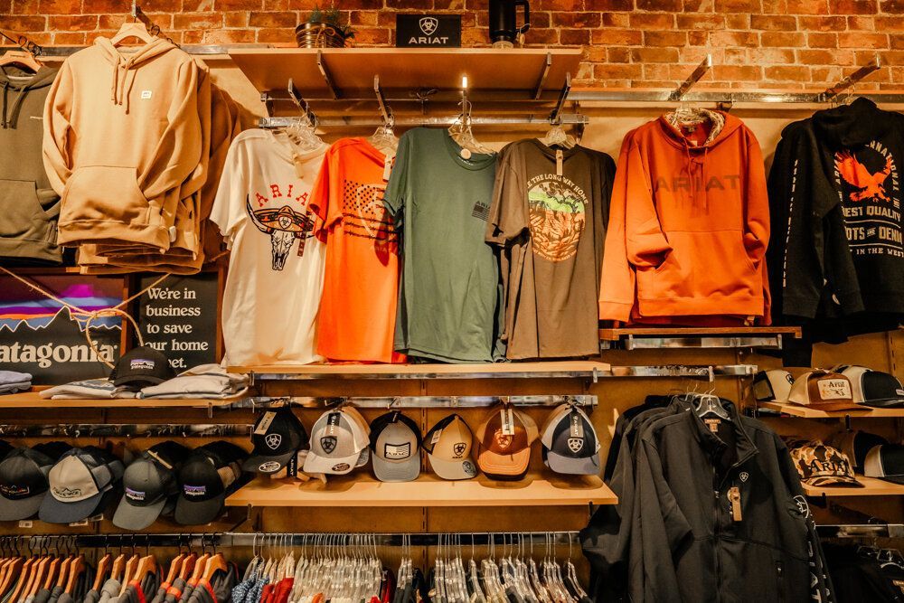 Clothing store interior: sweaters, shirts, hats, and jackets on display against a brick wall.