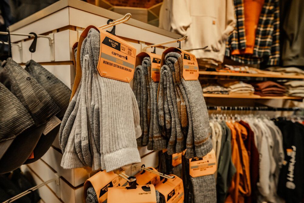 Socks and clothing on display in a store. Gray and brown socks hang from a rack with price tags.