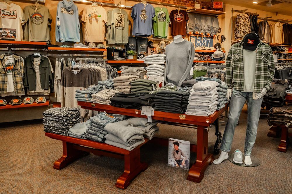 Clothing store interior with racks of shirts, jeans, and a mannequin wearing a plaid shirt.