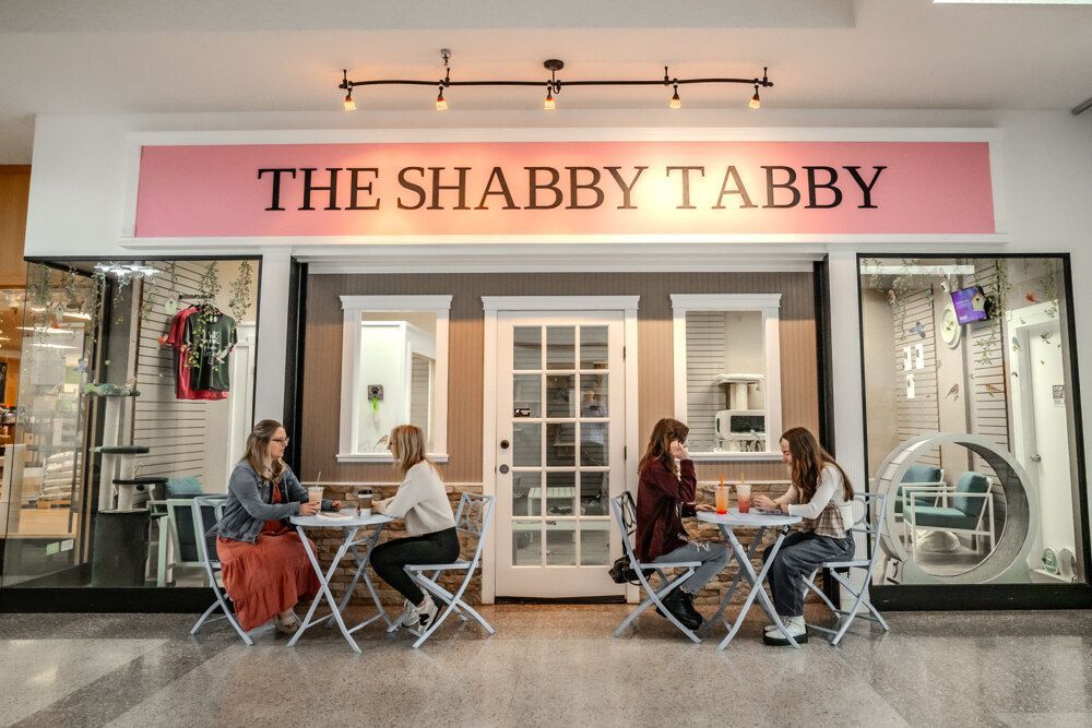 Four people seated at tables outside a shop called 