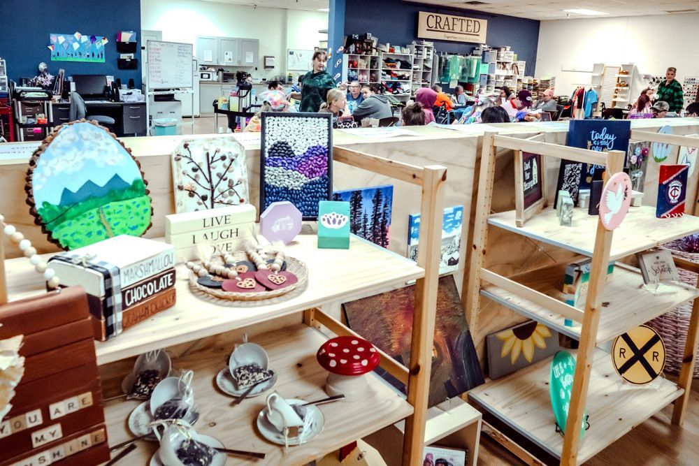 Inside a shop with wooden display shelves, displaying various handcrafted items like art, mugs, and decor.