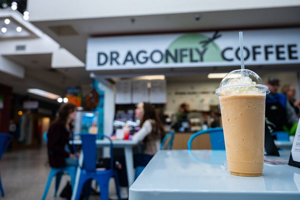 Frappe drink on table at Dragonfly Coffee shop, two women at a blue table in the background.