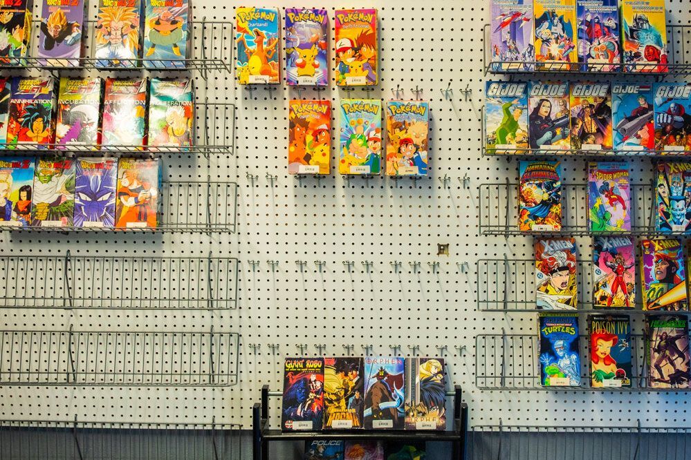 VHS tapes displayed on a pegboard with empty shelves below; cartoons and anime titles.