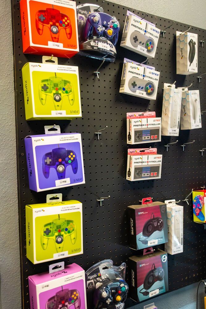A display of colorful game controllers in boxes hanging on a black pegboard.