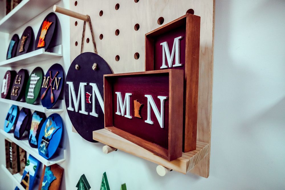 Display of Minnesota-themed wooden art pieces, including wall hangings and framed designs, in a shop setting.