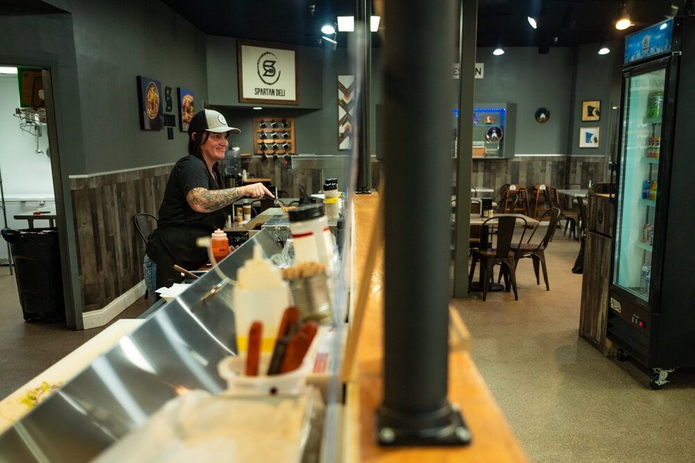 Person in a black shirt working behind a counter in a restaurant, preparing food.