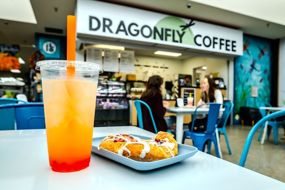 Orange drink and pastry on a table in front of Dragonfly Coffee shop; two people seated in background.