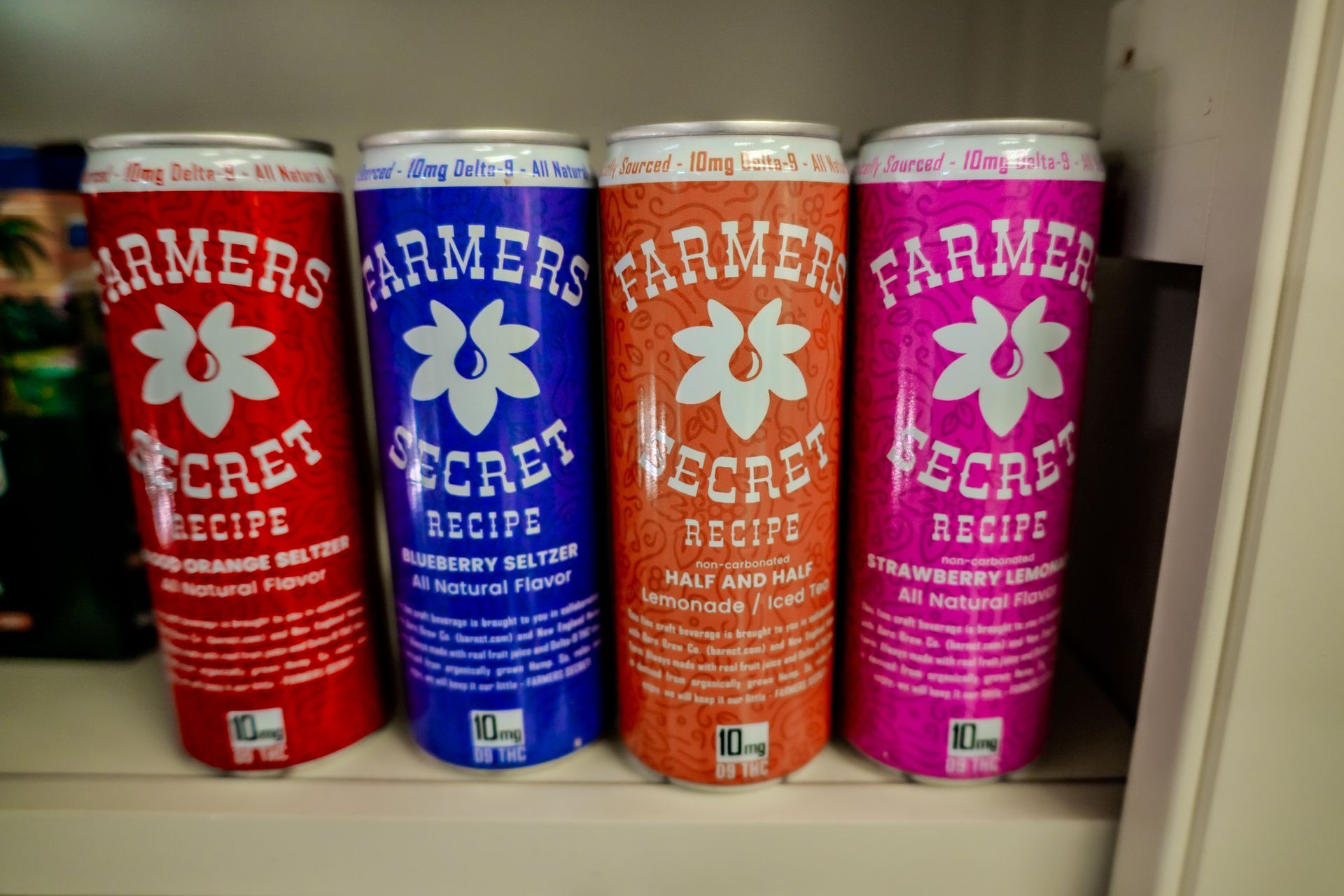 Four cans of Farmers Secret Recipe drinks, each a different color, lined up.