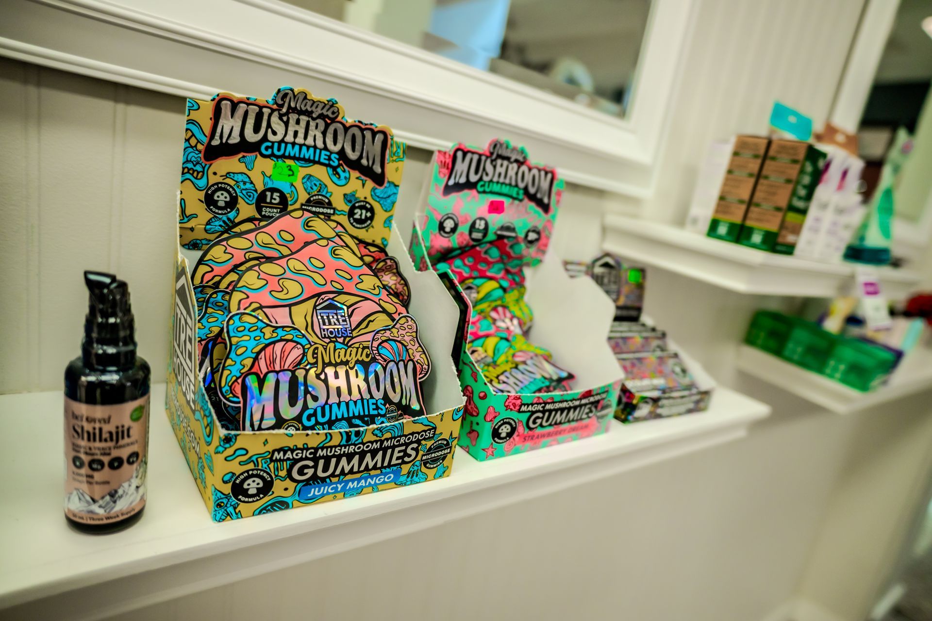 Shelf display with mushroom gummy boxes and a bottle of oil. Bright colors.