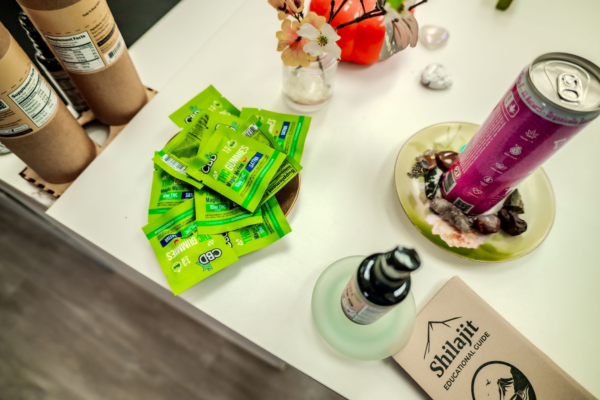 A table with green packets, a can, bottle, and flowers.