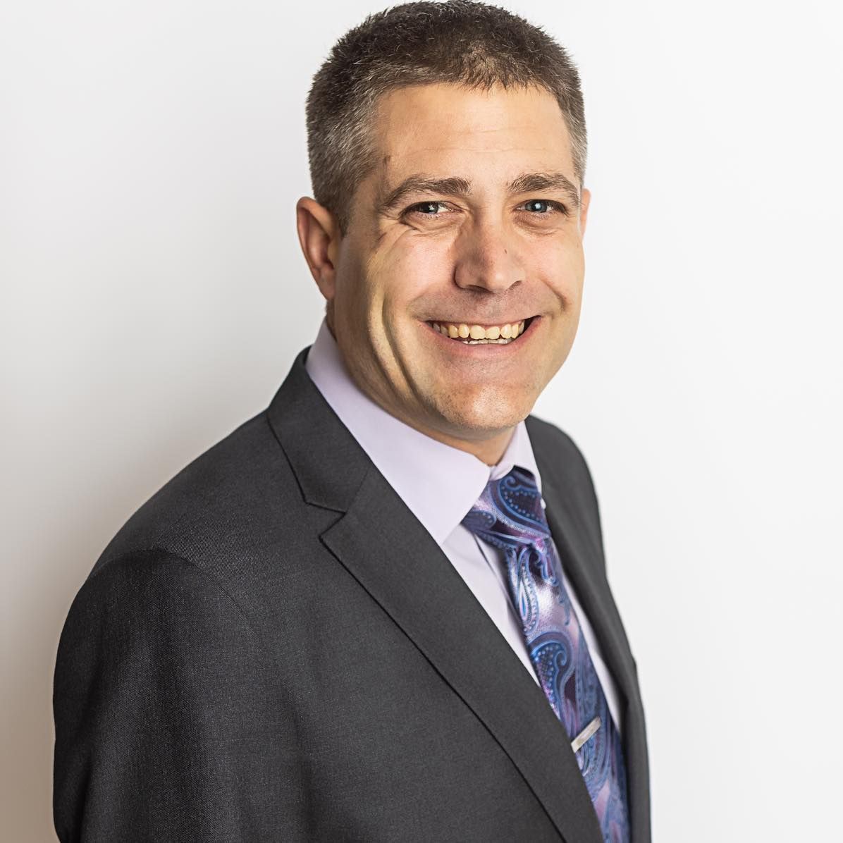 Man in suit smiles at the camera, light background.