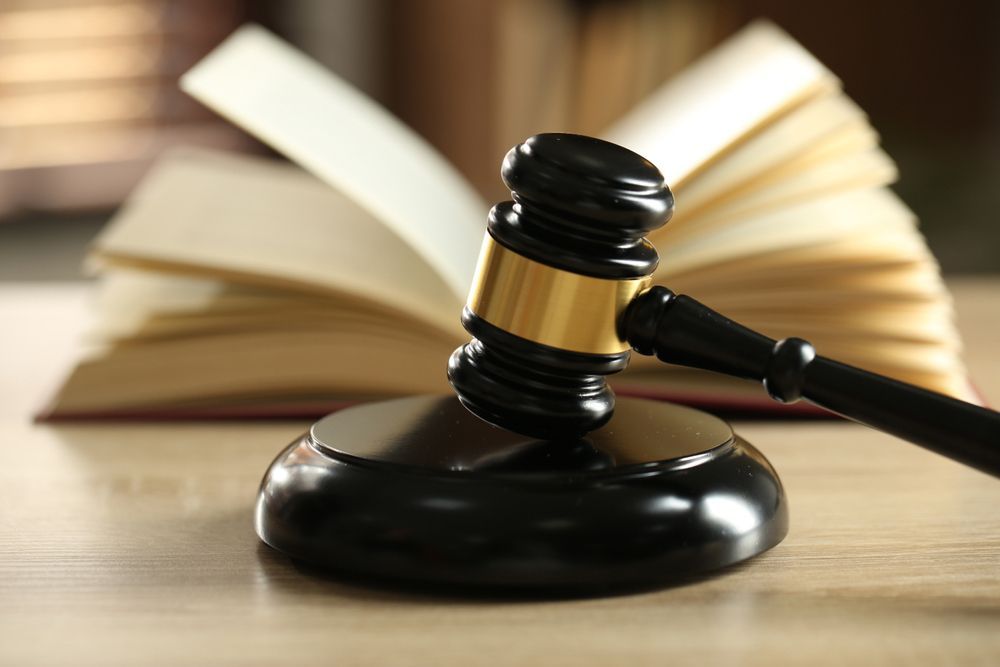 Gavel on sound block, with open book in background on a wooden surface.