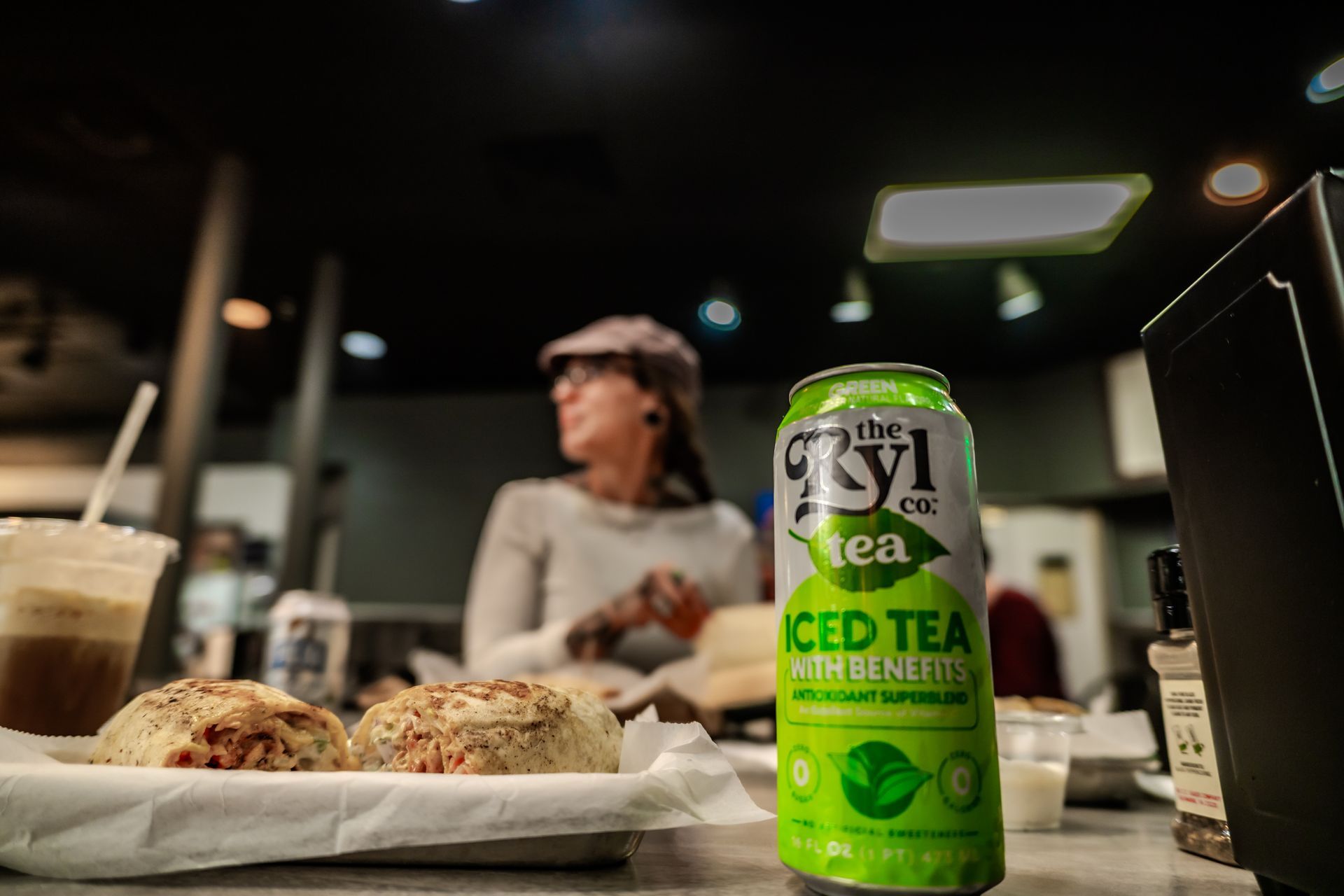 Green iced tea can, bagel and customer in a cafe.