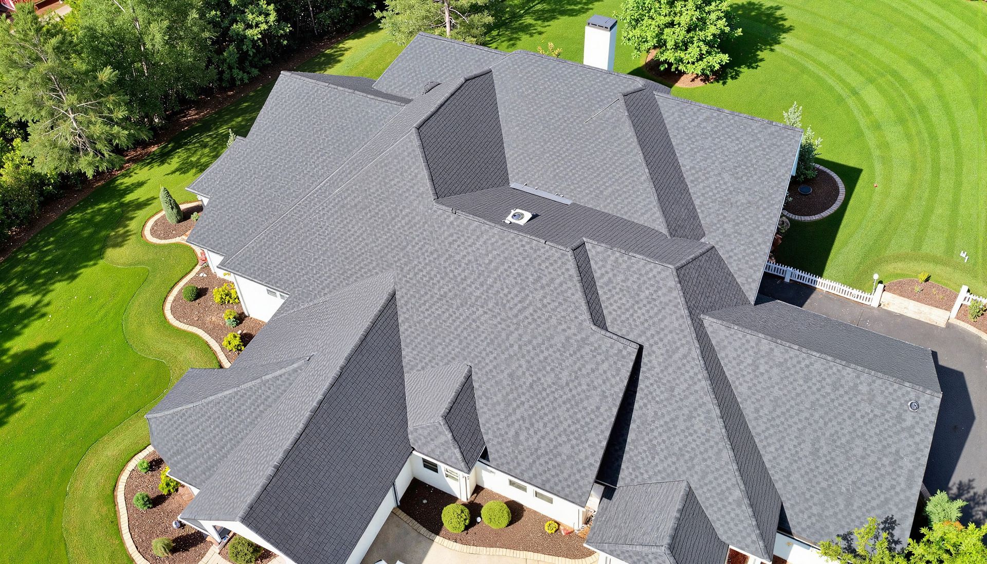 Aerial view of a large house with a gray roof surrounded by green lawn and landscaping