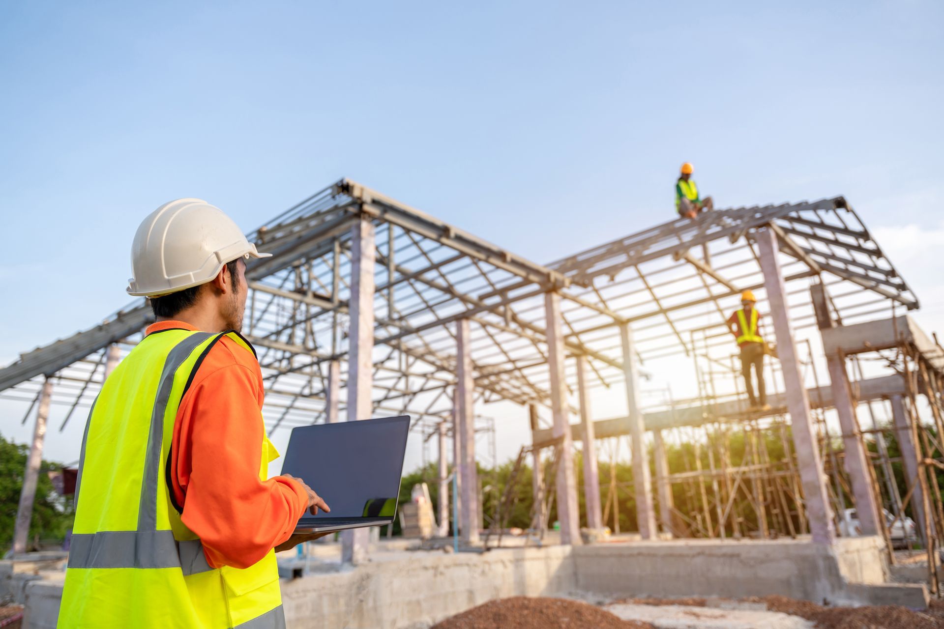 Construction workers in hard hats inspecting a steel frame building under construction at sunset