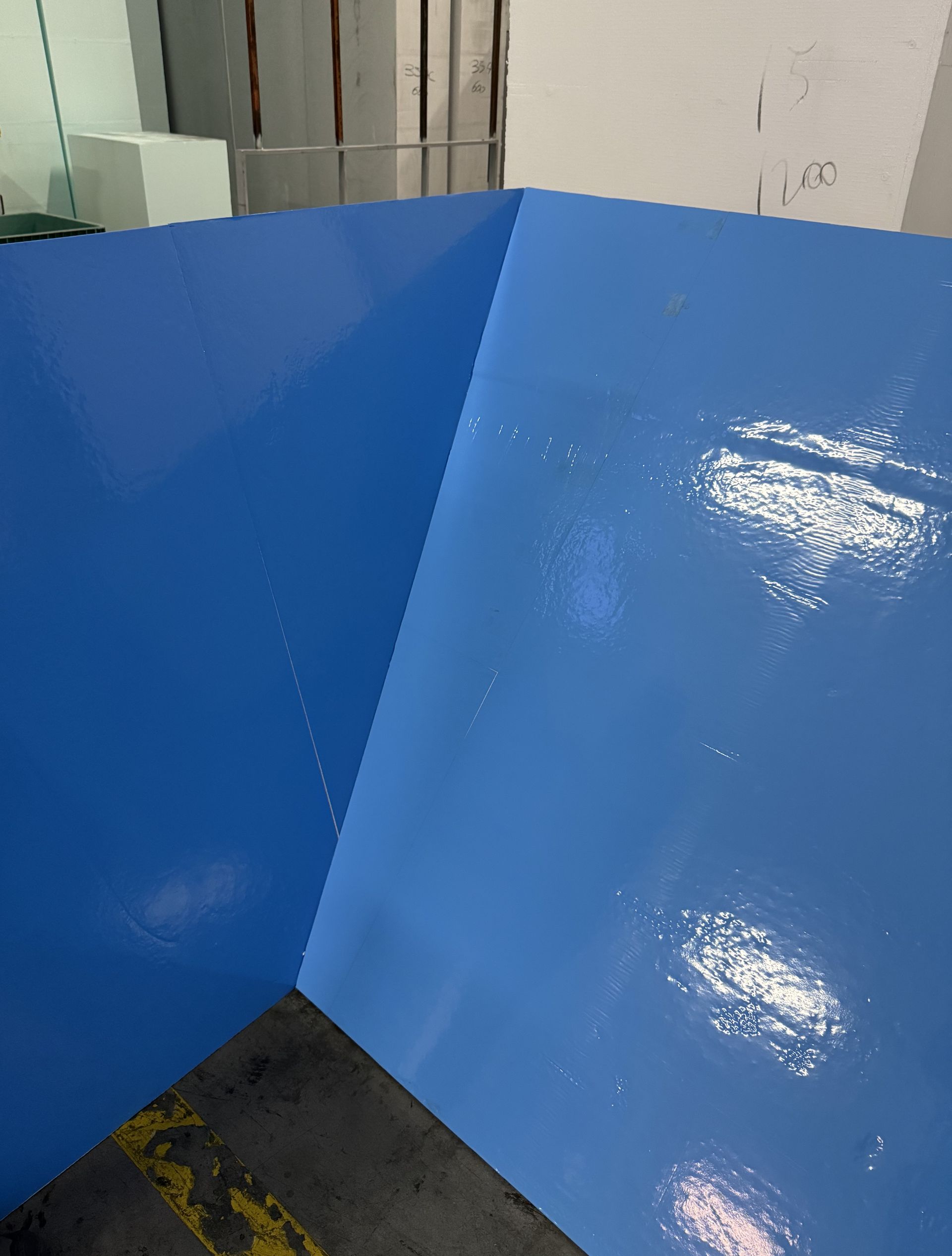 Pavimento industriale blu e lucido in un angolo. La luce si riflette, mostrando la texture.