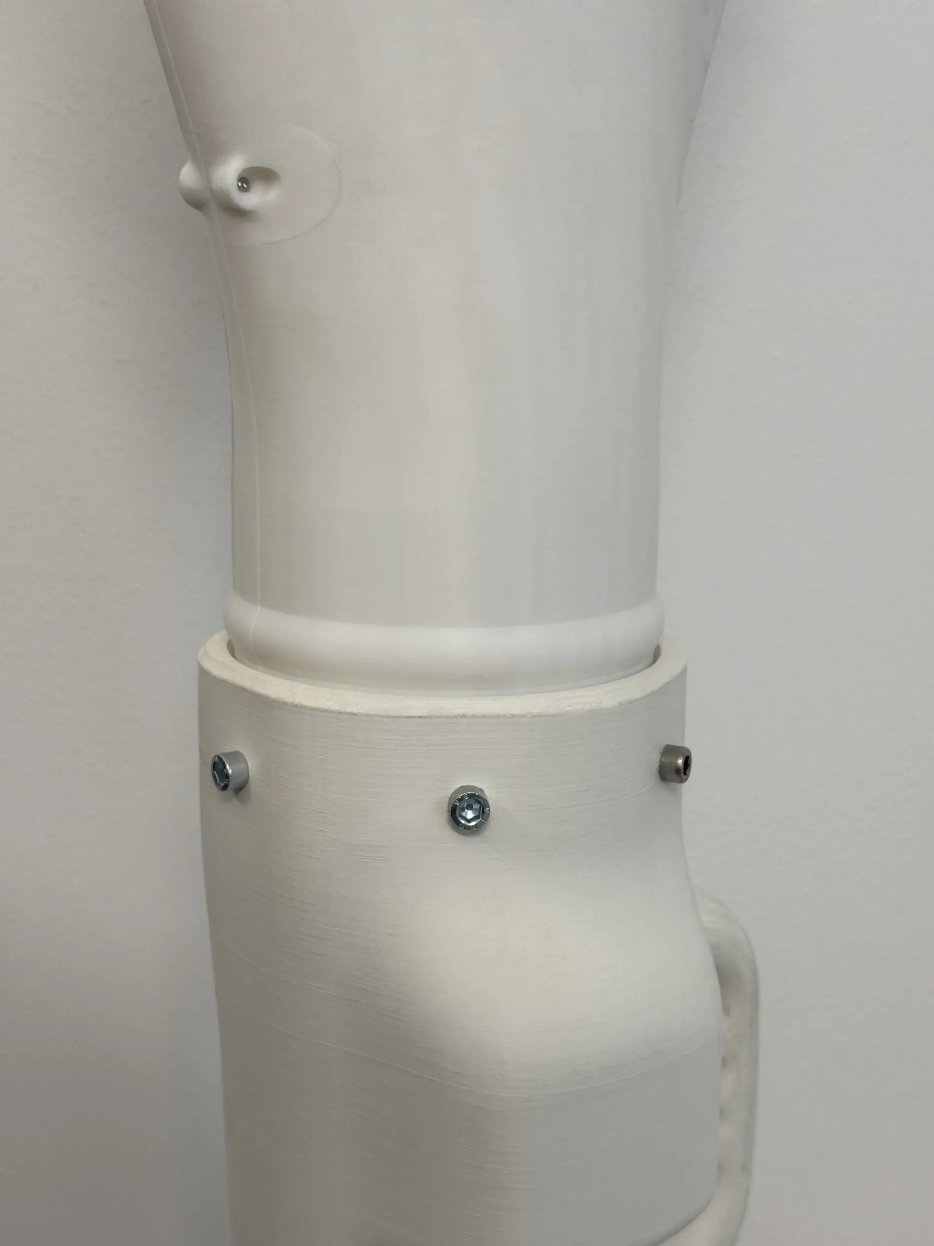 Segmento di braccio protesico bianco stampato in 3D con bulloni che fissano il bracciale alla parte superiore.