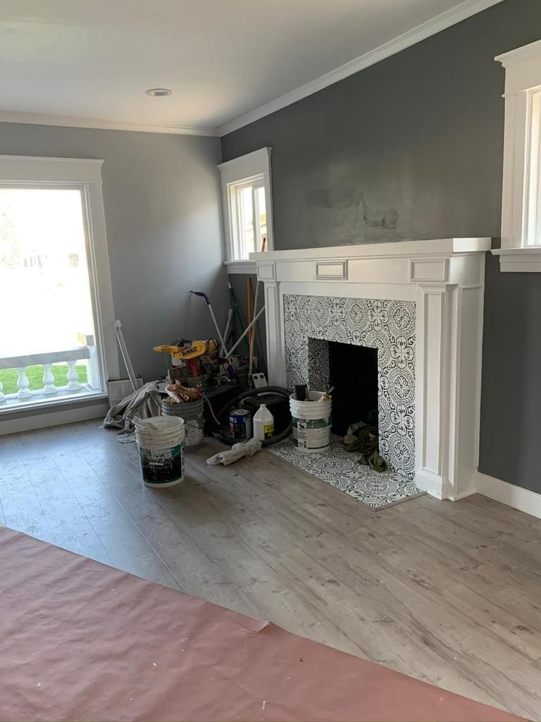A living room with a fireplace and a bucket of paint on the floor.