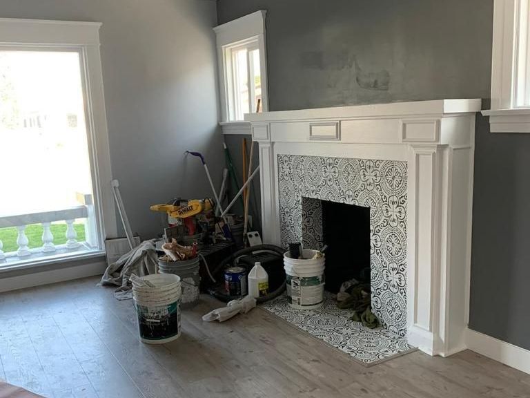A living room with a fireplace and buckets of paint.