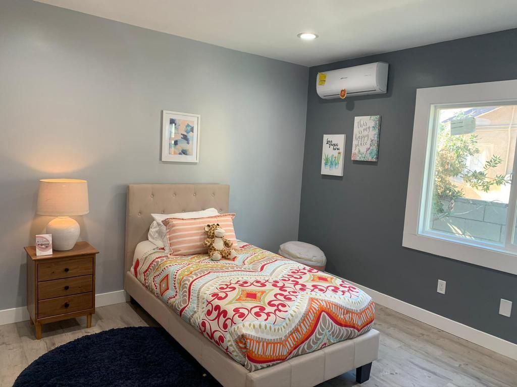 A bedroom with a single bed , nightstand , lamp and window.