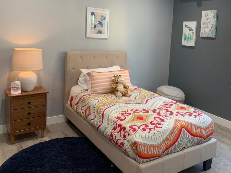 A bedroom with a single bed , nightstand , lamp and rug.