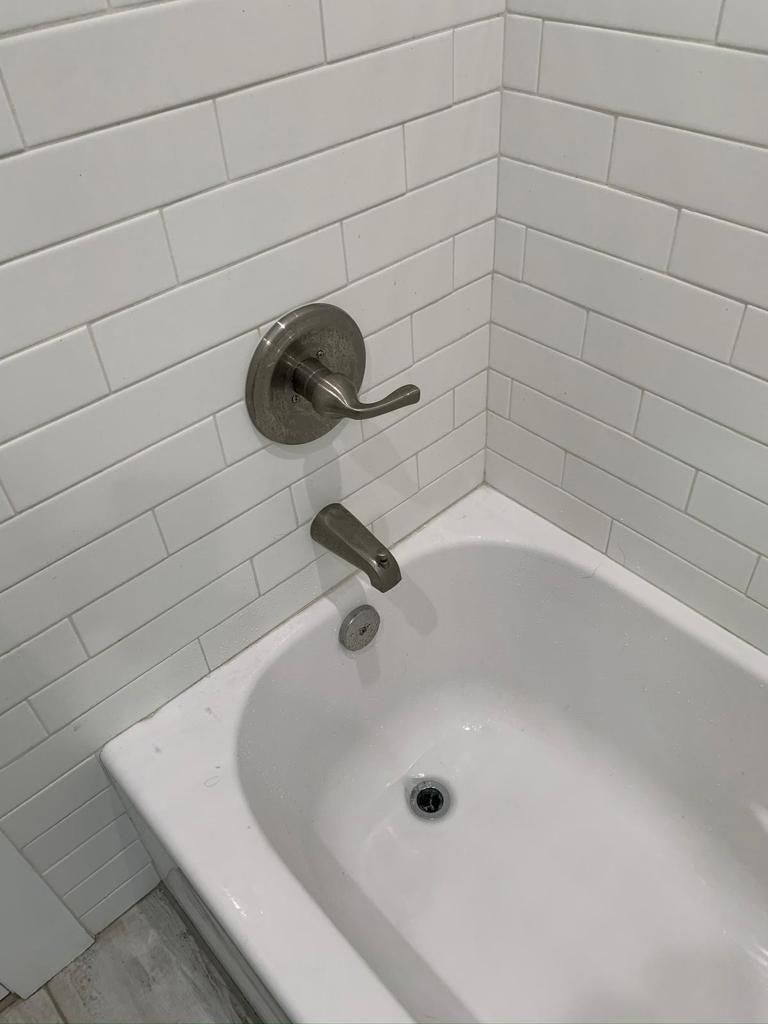 A bathtub in a bathroom with white tiles and a faucet.