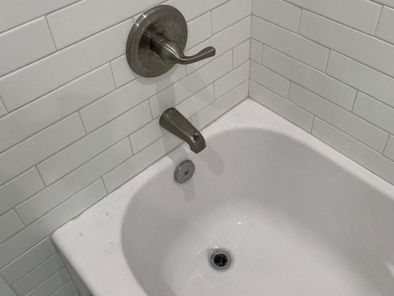 A bathtub in a bathroom with white tiles and a faucet.
