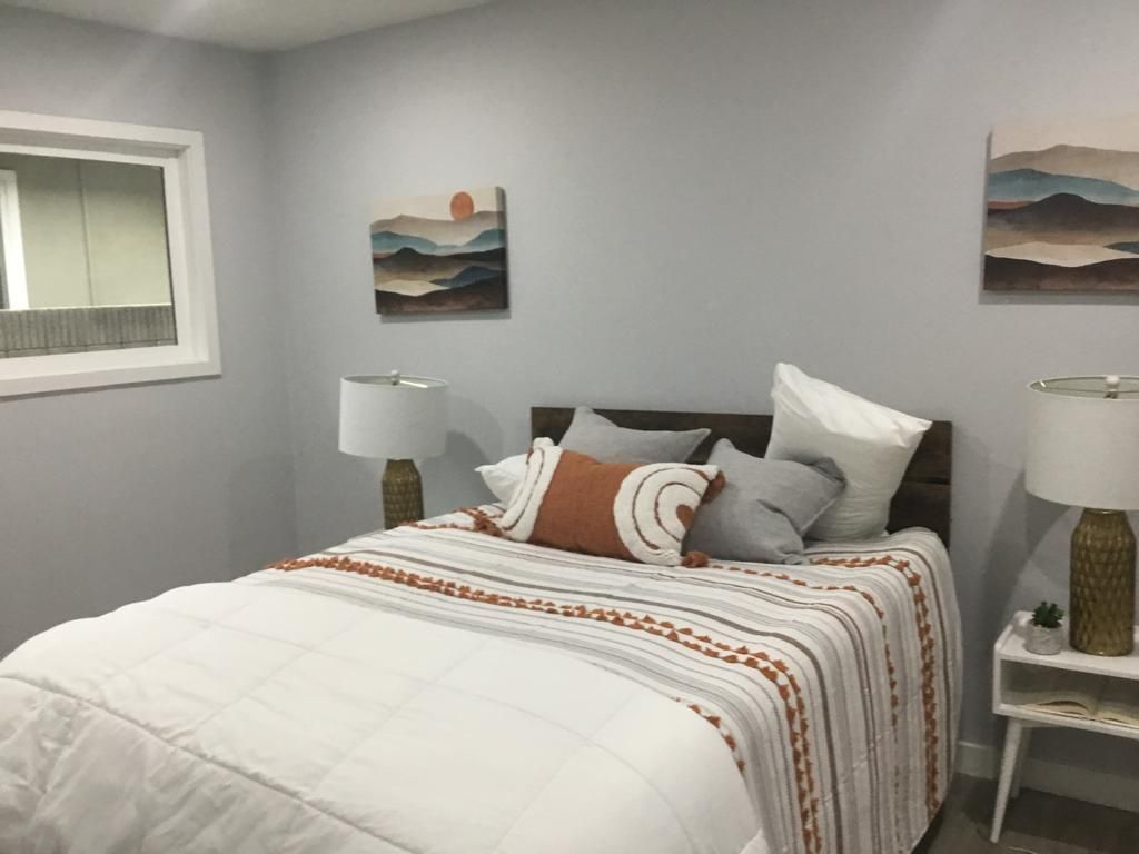 A bedroom with a bed , two lamps and two paintings on the wall.