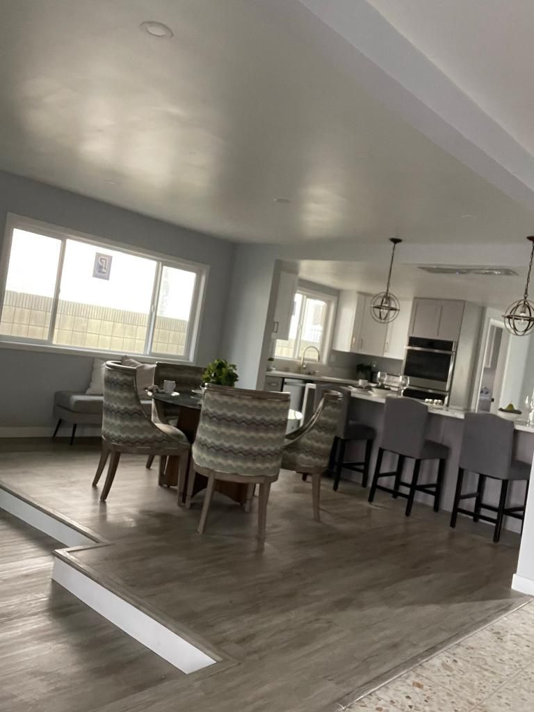 A dining room with a table and chairs and a kitchen in the background.