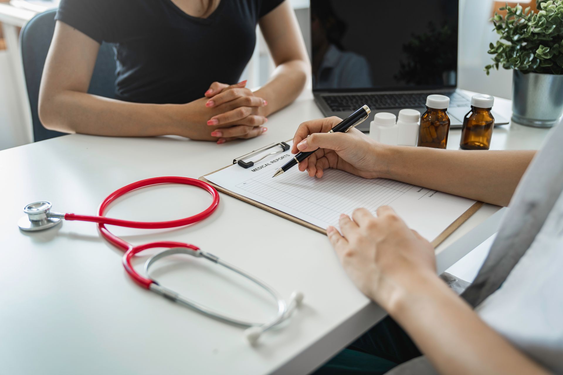 A doctor is sitting at a table with a patient and writing on a clipboard.