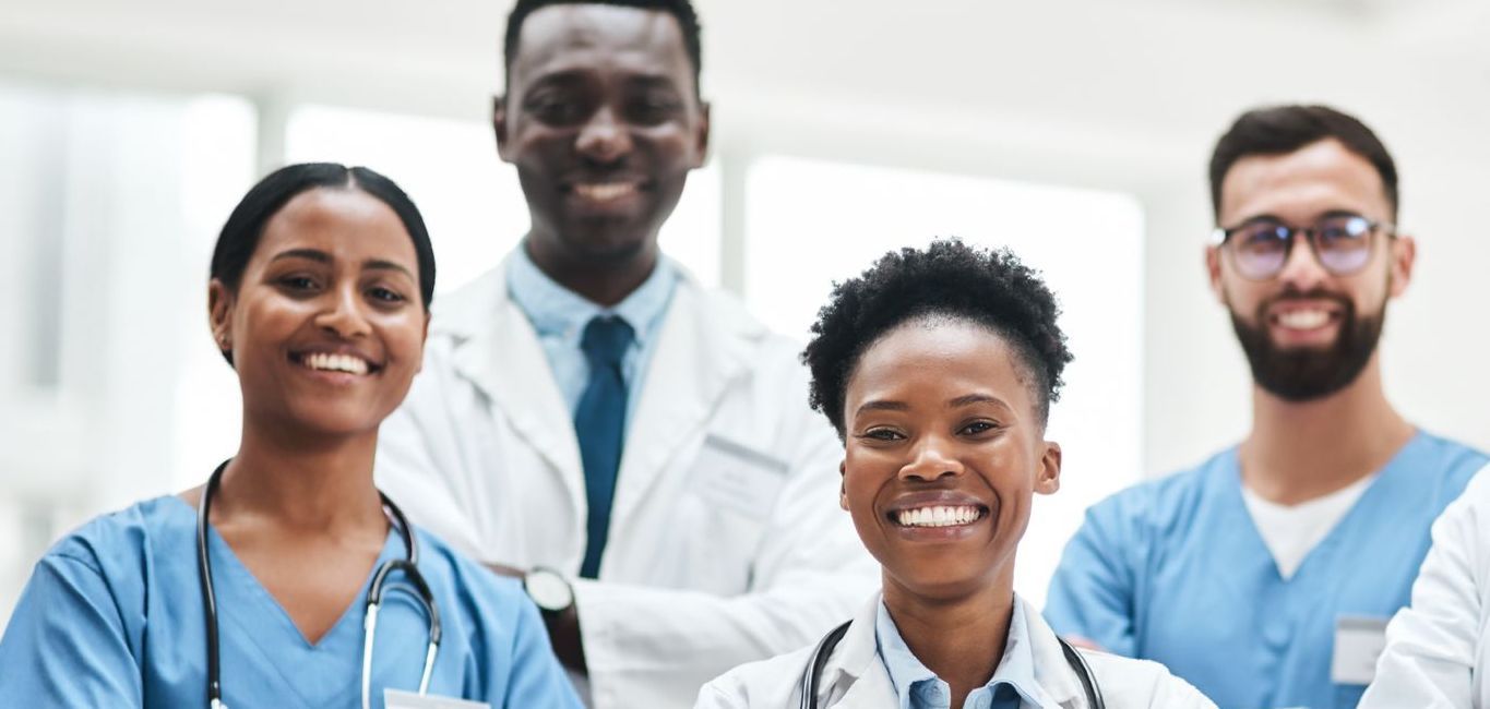 Two doctors are standing next to each other in a hospital hallway with their arms crossed.