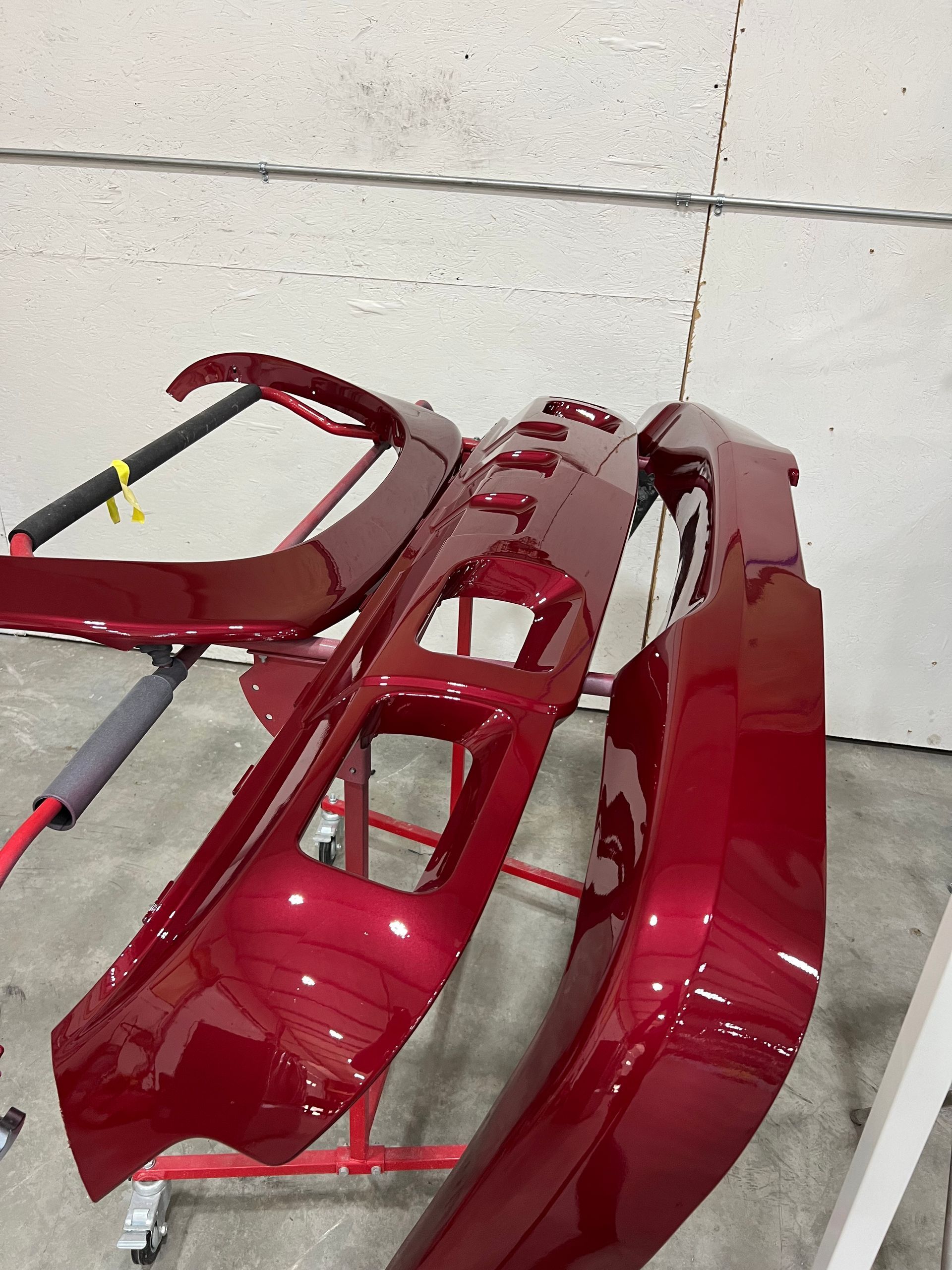 Red car body parts, freshly painted, hanging on a rack in a workshop.