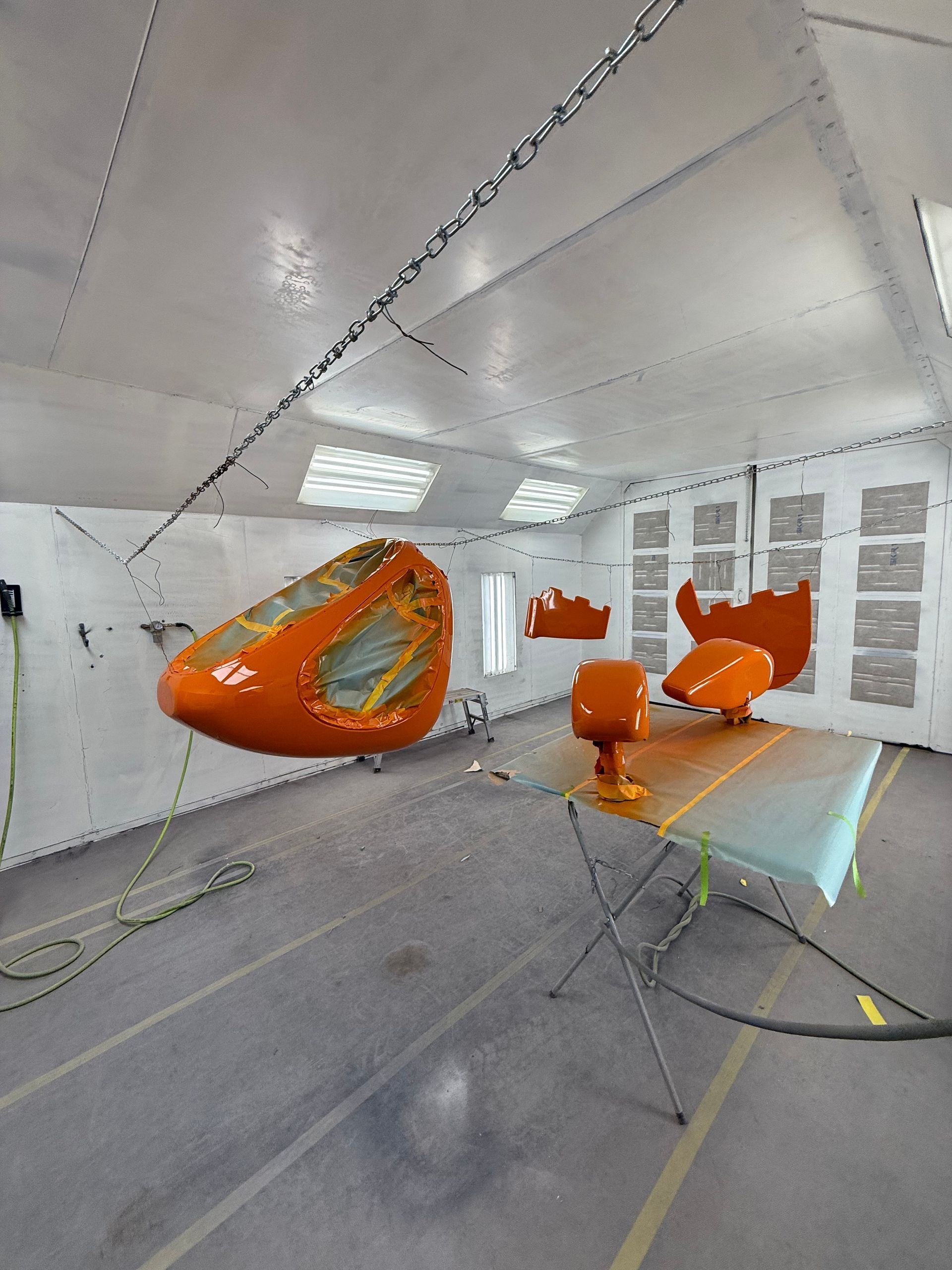 Orange vehicle parts suspended in a spray paint booth.