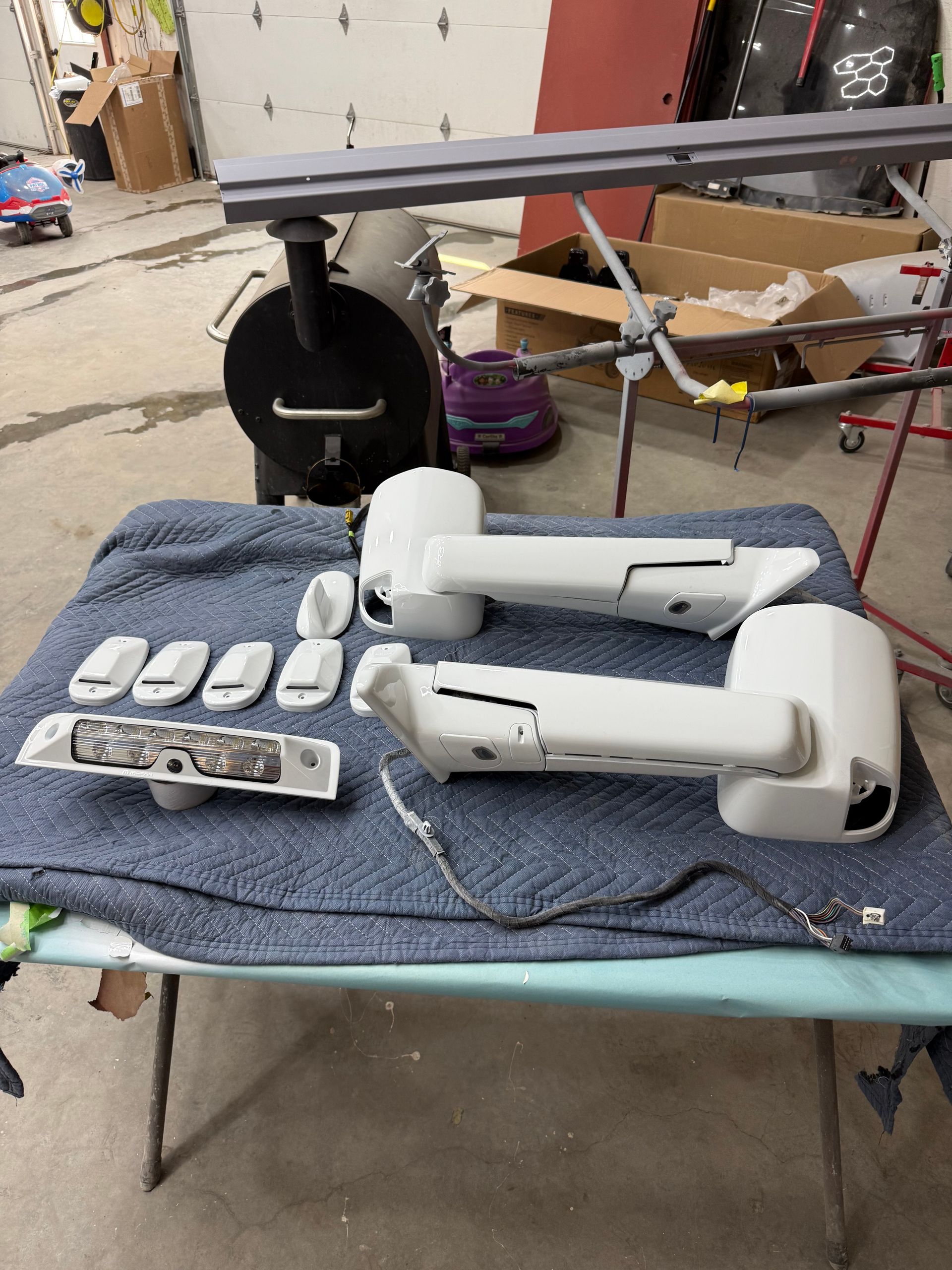 White vehicle side mirrors and related parts laid out on a table, ready for painting.