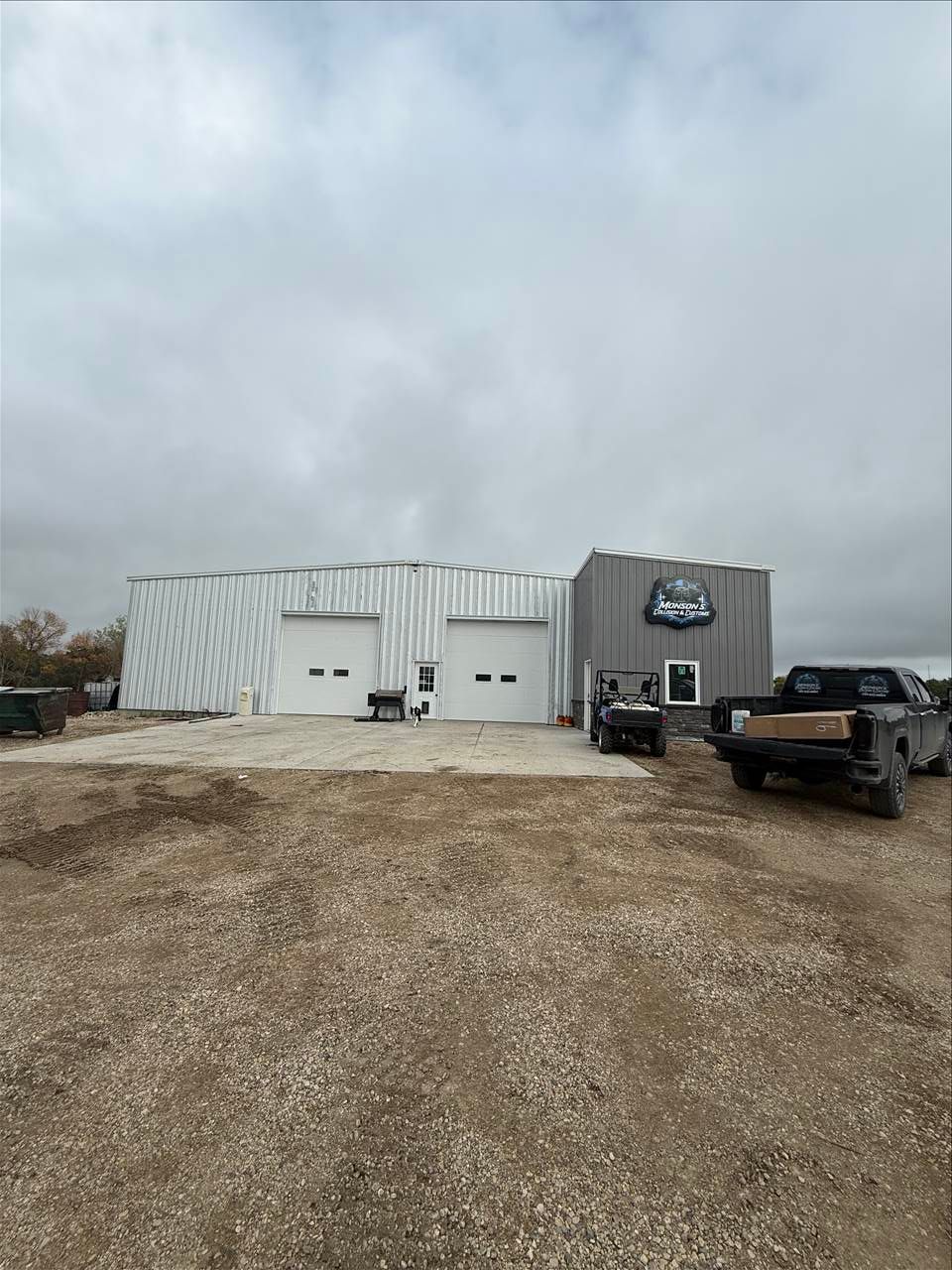 Building with garage doors, gravel lot, cloudy sky.