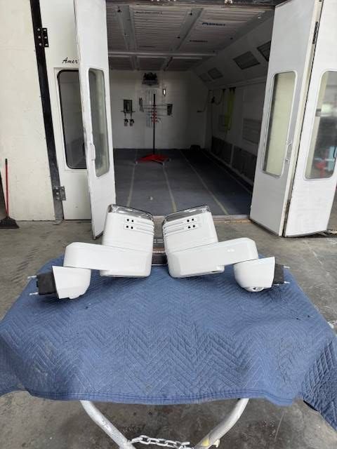 Two white truck side mirrors on a blue covered table in a paint booth.