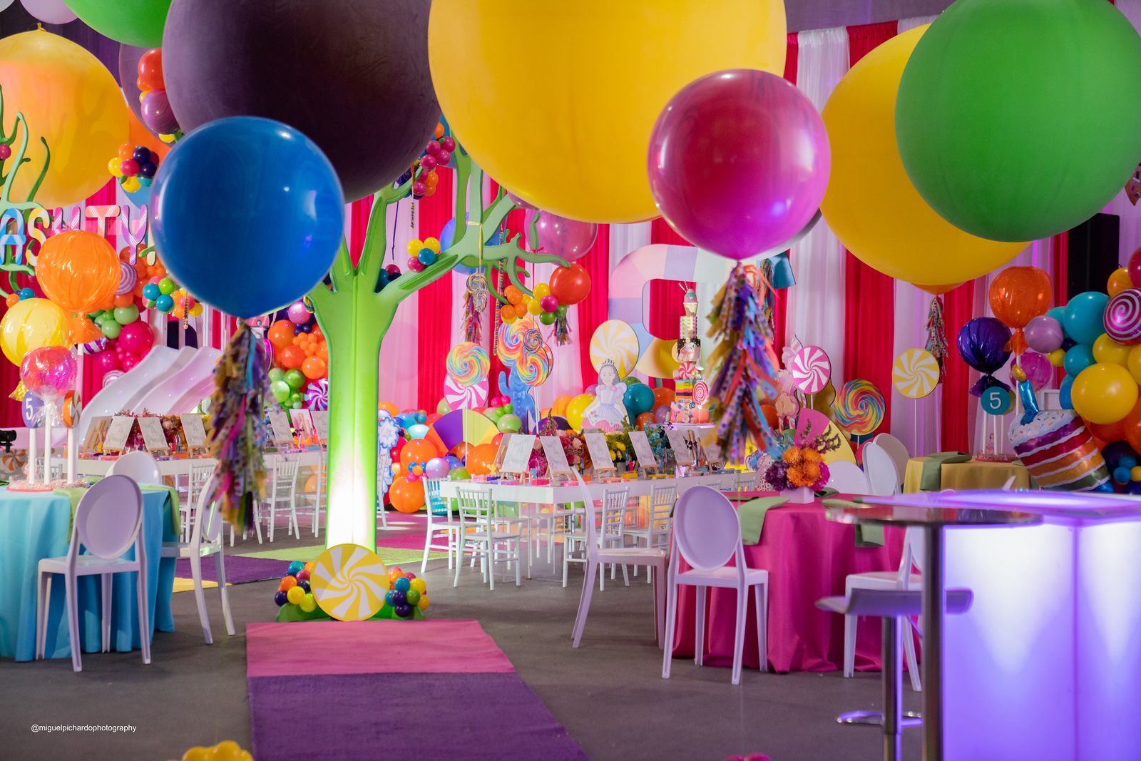 A room filled with colorful balloons and tables and chairs.
