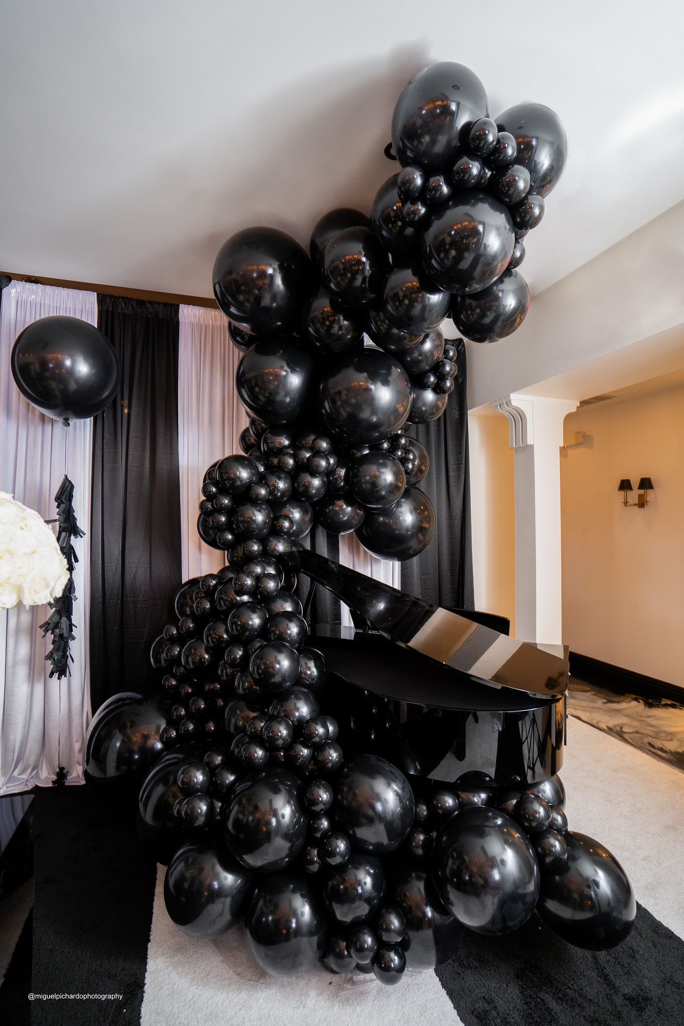A piano is surrounded by black balloons in a room.